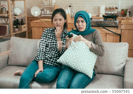 frowning girls watching horror movie on tv frowning girls watching horror movie on tv 55097591