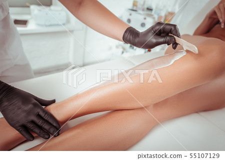 Attentive experienced cosmetologist working with wooden spatula Attentive experienced cosmetologist working with wooden spatula 55107129