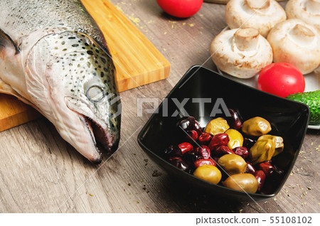 Close-up keta fish, whole on the cutting board of the kitchen table next to olives tomatoes and 55108102