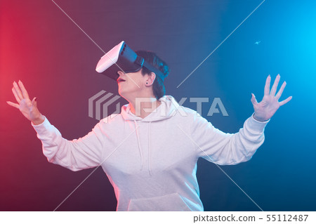 Middle-aged happy young woman using a virtual reality headset on red-blue background. 55112487