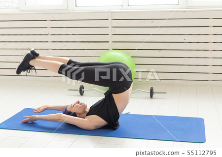 Young slim girl with colored hair makes an headstand on a sports blue mattress next to a barbell and Young slim girl with colored hair makes an headstand on a sports blue mattress next to a barbell and 55112795