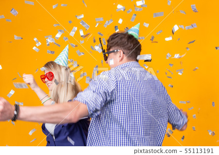 Fun, holidays and party concept - Couple dancing among falling confetti on yellow background Fun, holidays and party concept - Couple dancing among falling confetti on yellow background 55113191