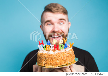 Crazy funny positive guy hipster holding a happy birthday cake in his hands standing on a blue 55115675