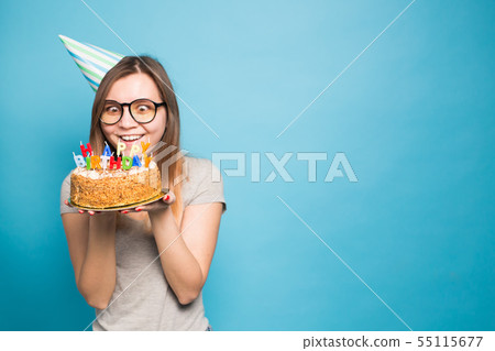 Cheerful young girl student in glasses holding a congratulatory cake with a candle standing on a 55115677