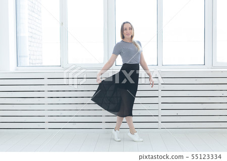 Youth, style and people concept - young woman on black skirt and sneakers standing near the window Youth, style and people concept - young woman on black skirt and sneakers standing near the window 55123334