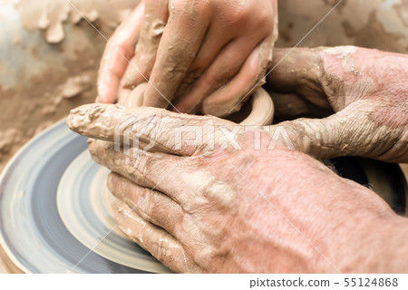 two pairs of hands mold something from clay on a 55124868