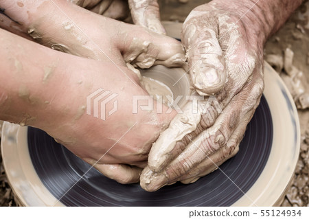 two pairs of hands mold something from clay on a 55124934