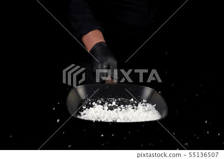 Chef in black uniform holds a pan with white salt Chef in black uniform holds a pan with white salt 55136507