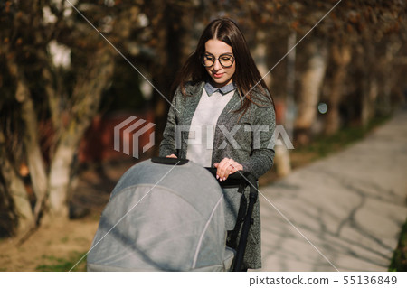 Young mom walking with stroller in the park. Stylish mother with baby 55136849
