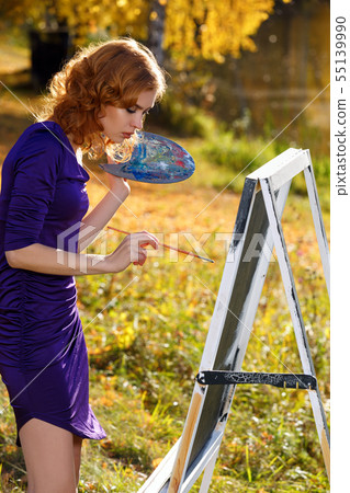 Young woman in sexy dress painting outdoors in autumn park. Young woman in sexy dress painting outdoors in autumn park. 55139990
