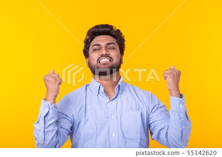 Young Indian brunette male rejoices posing on a yellow background. Concept of success and win. Young Indian brunette male rejoices posing on a yellow background. Concept of success and win. 55142620