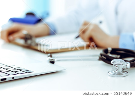 Closeup of stethoscope. Female doctor fills up medical form while sitting at the desk in hospital 55143649