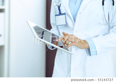 Doctor woman using tablet in clinic office. Unknown female physician at work while standing straight Doctor woman using tablet in clinic office. Unknown female physician at work while standing straight 55143727