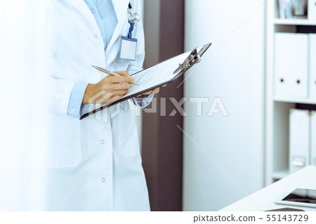 Doctor woman filling up medical form in clinic office. Unknown female physician at work while Doctor woman filling up medical form in clinic office. Unknown female physician at work while 55143729