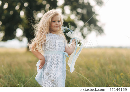 Little girl in sky blue dress stand in field in front of big tree 55144169