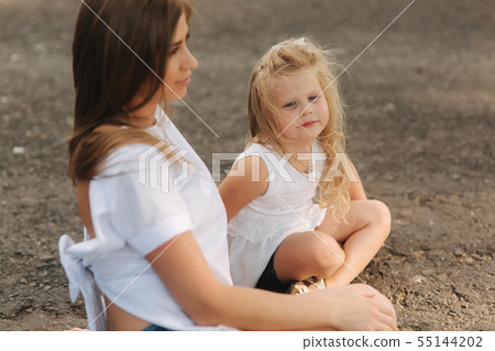 Attractive Mom and blonde hair daughter sits on road near big alley. They smile and look to natune 55144202