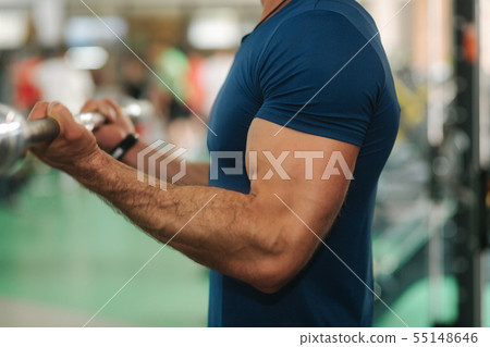 Close up of young athlete trains in the gym. Trians biceps muscules using barbell 55148646