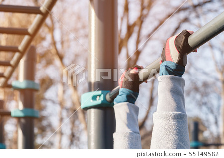 Close-up of female hands in sport gloves are holding onto a horizontal bar. Female workout concept Close-up of female hands in sport gloves are holding onto a horizontal bar. Female workout concept 55149582