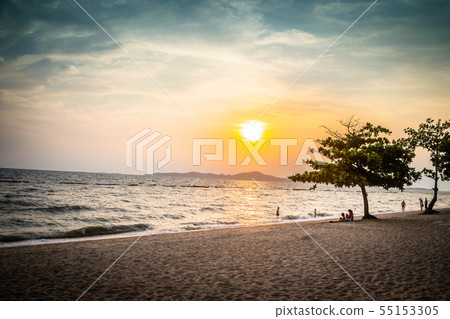 Beautiful blue orange sunset by the sea and a lonely standing tree and walking people 55153305