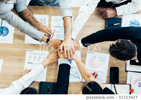 Colleagues stacking hands above table with papers Colleagues stacking hands above table with papers 55153427