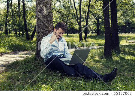 Young man working on his laptop in a public park Young man working on his laptop in a public park 55157062