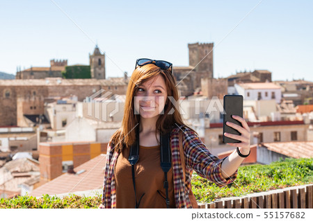 A young red-haired tourist makes a selfie from the viewpoint of Galarza with the old town of Caceres A young red-haired tourist makes a selfie from the viewpoint of Galarza with the old town of Caceres 55157682