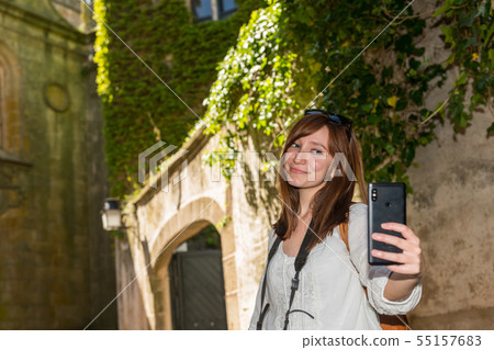 A young red-haired tourist makes a selfie next to a tower covered in green ivy in the old town of A young red-haired tourist makes a selfie next to a tower covered in green ivy in the old town of 55157683
