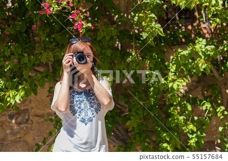A young woman with reddish hair takes photographs with her camera next to a wall covered with A young woman with reddish hair takes photographs with her camera next to a wall covered with 55157684