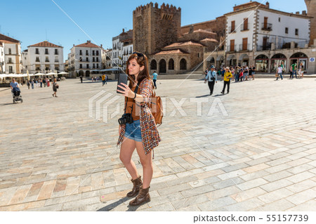 A young red-haired tourist with a backpack makes a selfie in the Plaza Mayor de Caceres A young red-haired tourist with a backpack makes a selfie in the Plaza Mayor de Caceres 55157739