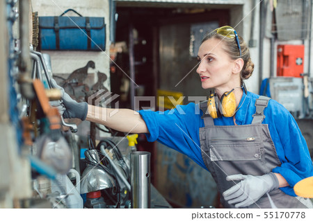 Metalworker woman in workshop grabbing tool 55170778