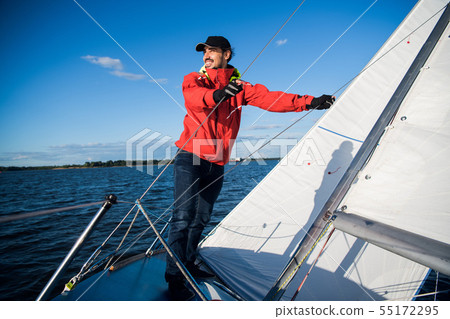 Low angle view of sailor operating windlass on yacht. Working with ropes and sail Low angle view of sailor operating windlass on yacht. Working with ropes and sail 55172295