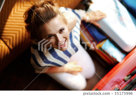 smiling young woman packing stuff in open travel suitcase 55173996
