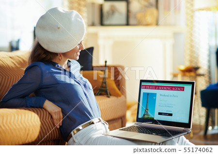 woman in white beret looking at online travel site on laptop 55174062