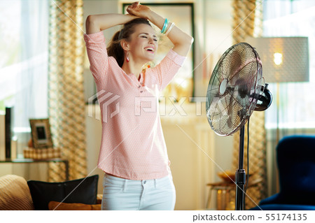 smiling young woman enjoying breeze in front of fan 55174135