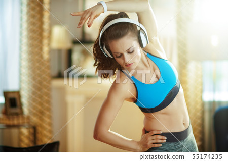 young woman in headphones at modern home stretching young woman in headphones at modern home stretching 55174235