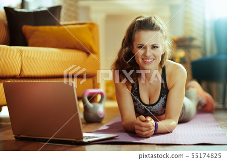 sports woman with laptop laying on fitness mat in modern house 55174825
