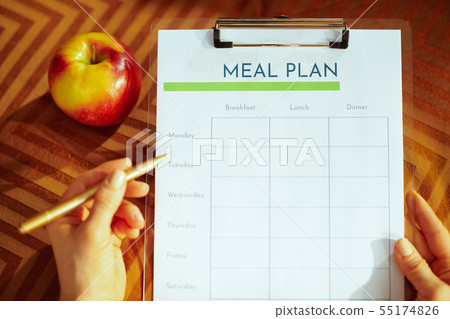 Closeup on female hands holding clipboard and filling meal plan Closeup on female hands holding clipboard and filling meal plan 55174826