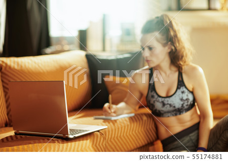 Closeup on laptop and active woman in background taking notes Closeup on laptop and active woman in background taking notes 55174881
