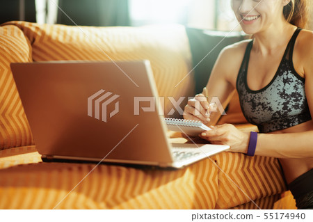 Closeup on woman with notepad and pen taking notes while using o 55174940