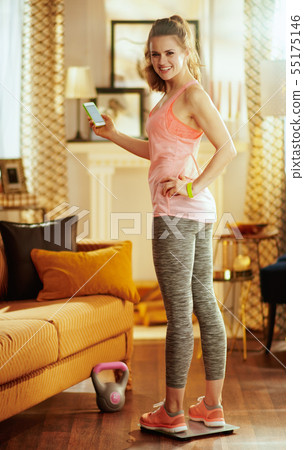 sports woman standing at smart scale and with a smartphone 55175146