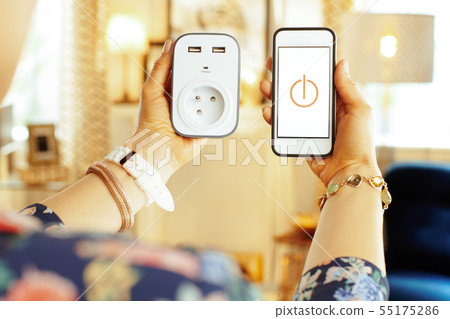 Closeup on smartphone with smart home app and plug in hand Closeup on smartphone with smart home app and plug in hand 55175286