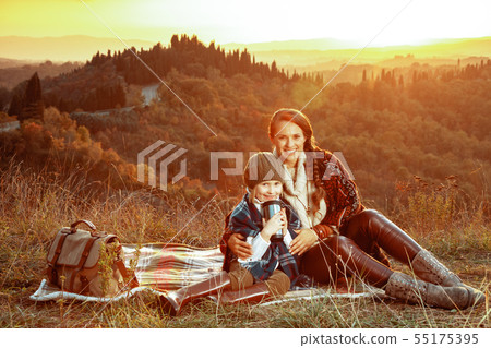 smiling mother and daughter sitting on blanket with thermos cup 55175395