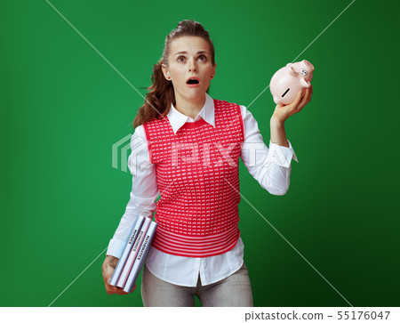 learner woman with textbooks shaking pink piggy bank and looking learner woman with textbooks shaking pink piggy bank and looking 55176047