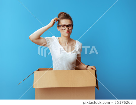 pensive modern woman in white t-shirt in cardboard box on blue pensive modern woman in white t-shirt in cardboard box on blue 55176263