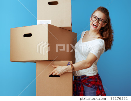 smiling modern woman holding pile of cardboard boxes on blue 55176331