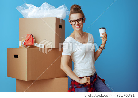smiling modern woman near cardboard box with coffee cup on blue 55176381