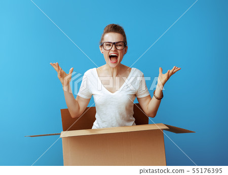 happy modern woman pops out of cardboard box on blue 55176395