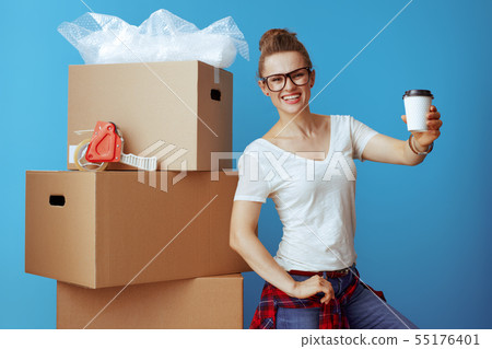 smiling woman near cardboard box giving coffee cup on blue 55176401
