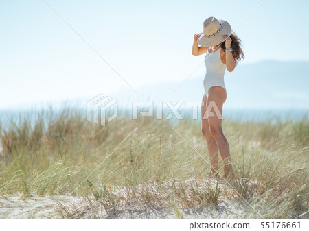 modern woman in white swimsuit on ocean coast wearing hat modern woman in white swimsuit on ocean coast wearing hat 55176661
