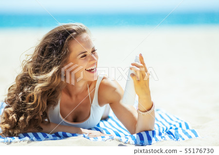 happy woman applying SPF while laying on striped towel 55176730